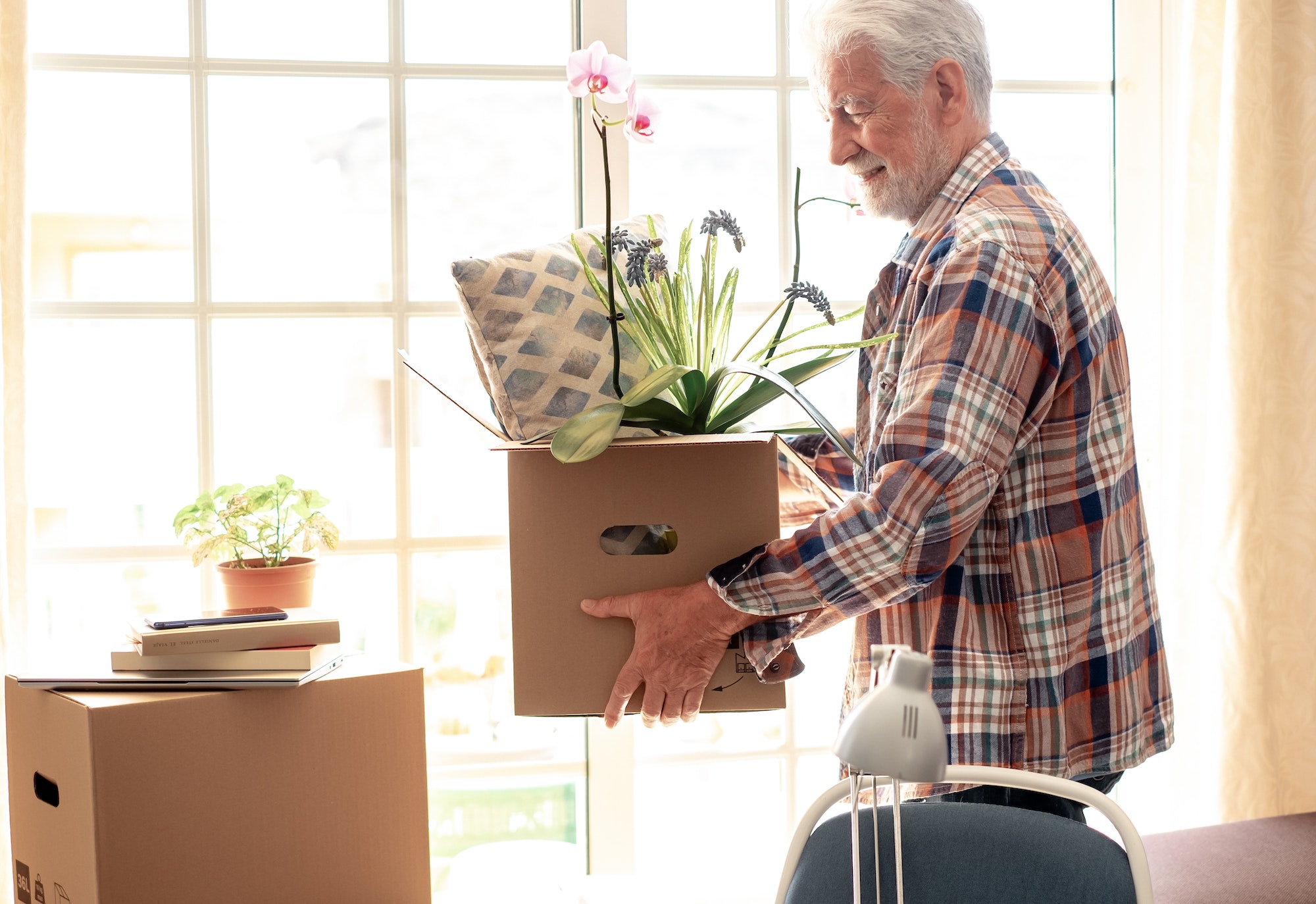 Hipster handsome senior man holding cardboard box in new house in moving day, concept of relocation